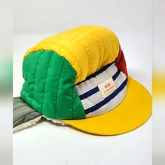 a yellow and green hat sitting on top of a pile of clothing next to a white wall