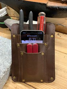 a cell phone in a leather case with some pens and pencils sticking out of it