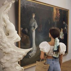 a woman standing in front of a painting and holding a wicker basket with her back to the camera