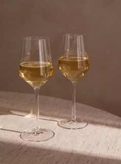 two glasses of wine sitting on top of a table next to each other with one glass filled with liquid