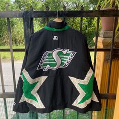 a black jacket with green and white stars hanging on a fence next to a potted plant