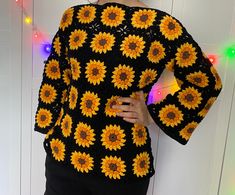 a woman standing in front of a wall wearing a black and yellow crochet top with sunflowers on it