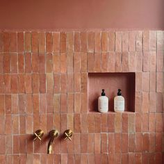 two soap dispensers on the side of a brick wall in a bathroom