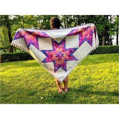 a woman is walking in the grass with a quilted star on her shawl