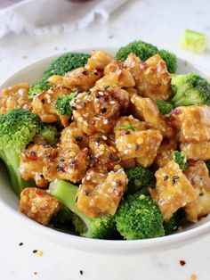 a white bowl filled with chicken and broccoli covered in sesame seed flakes