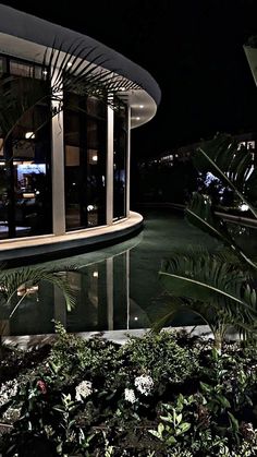 the pool is surrounded by greenery and plants at night time, with lights on