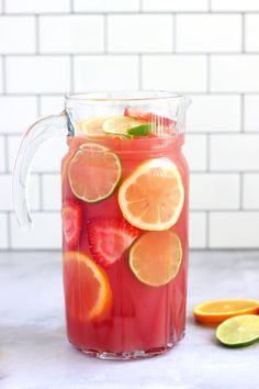 a pitcher filled with liquid and sliced oranges next to slices of lime on the counter