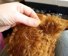 a person is holding the end of a brown teddy bear's hair as it sits in front of a sewing machine