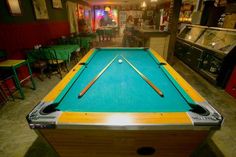 a pool table in the middle of a room with green chairs and tables around it