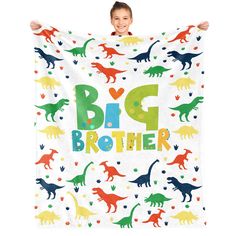 a little boy holding up a big brother towel with dinosaurs all over it and hearts