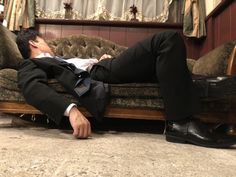 a man in a suit and tie laying on a couch with his feet propped up