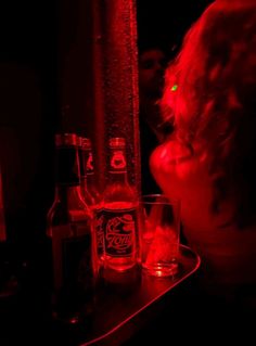 a woman sitting at a table with two bottles and glasses in front of her on the counter