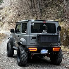 a grey jeep parked on the side of a road next to a lush green forest