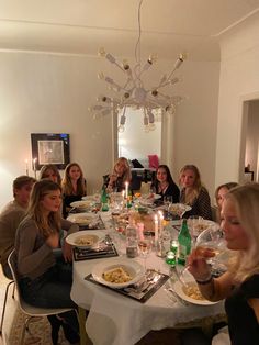 a group of people sitting around a dinner table eating food and drinking wine with candles in the middle