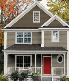 a gray house with white trim and red door in the front yard on a fall day