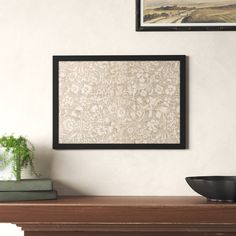 a wooden table topped with a bowl filled with green plants next to a painting on the wall