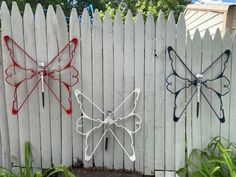 two metal butterfly sculptures on the side of a white fence