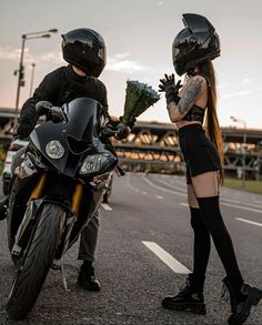 a man and woman standing next to each other on the street with motorcycle helmets on