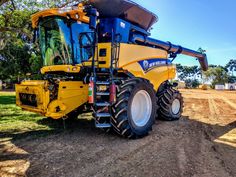 a large yellow and blue tractor parked on top of a dirt field