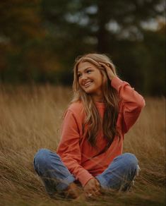 a woman sitting in the grass with her hands behind her head and smiling at the camera