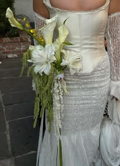 a woman in a white dress holding a bouquet of flowers on her shoulder and wearing an off the shoulder corset