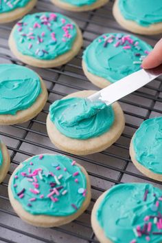 someone is spreading blue icing on some cookies