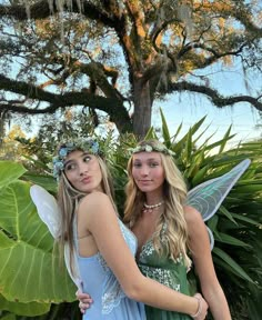 two girls dressed as tinkerbells standing next to each other in front of a tree