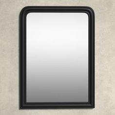 a black framed mirror on a wall with a light gray concrete floor and walls behind it