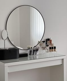 a white table topped with a round mirror and lots of makeup on top of it