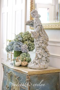 there is a statue on top of a dresser next to some flowers and pumpkins