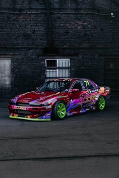 a colorful car parked in front of a brick building with graffiti on it's side