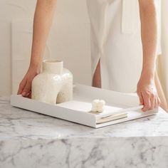 a person standing over a table with a white vase on it and some books in front of them