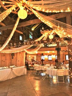 the inside of a barn decorated for a wedding reception with lights and draping