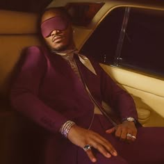 a man in a purple suit sitting next to a car wearing a blind folded headband