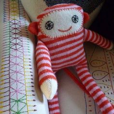 a red and white striped sock monkey laying on top of a bed next to a pillow