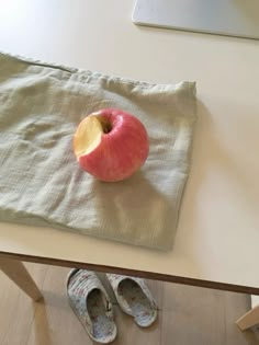 an apple sitting on top of a white table next to a pair of slippers