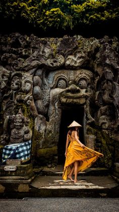 a woman in a yellow dress and straw hat walks into a doorway with carvings on it