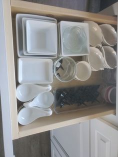 an open cabinet filled with white dishes and spoons