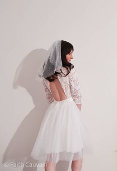 a woman in a white dress and veil is standing against a wall with her back to the camera