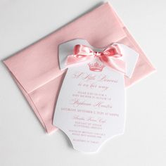 a pink and white baby shower with a bow on it's headband, sitting next to an envelope