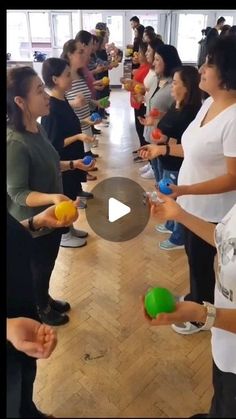 a group of people standing around each other in a room with balls on the floor