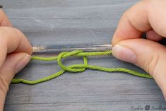 two hands are tying a green rope on a piece of wood with one hand and the other