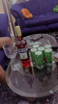 a glass table topped with bottles and glasses next to a purple couch in a living room