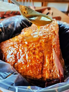 a spoon is pouring honey onto a piece of meat in a foil container with blue wrappers