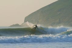 a man riding a wave on top of a surfboard in the ocean next to a cliff