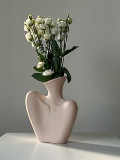 a white vase with flowers in it sitting on a table next to a gray wall