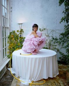 a woman in a pink dress sitting on top of a table with a white cloth