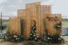 a bamboo structure with flowers and plants on the sides, in front of a fence