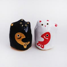 two ceramic cats sitting next to each other on a white surface with one black cat and one red cat