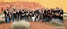 a large group of people standing in front of a rock formation with mountains in the background